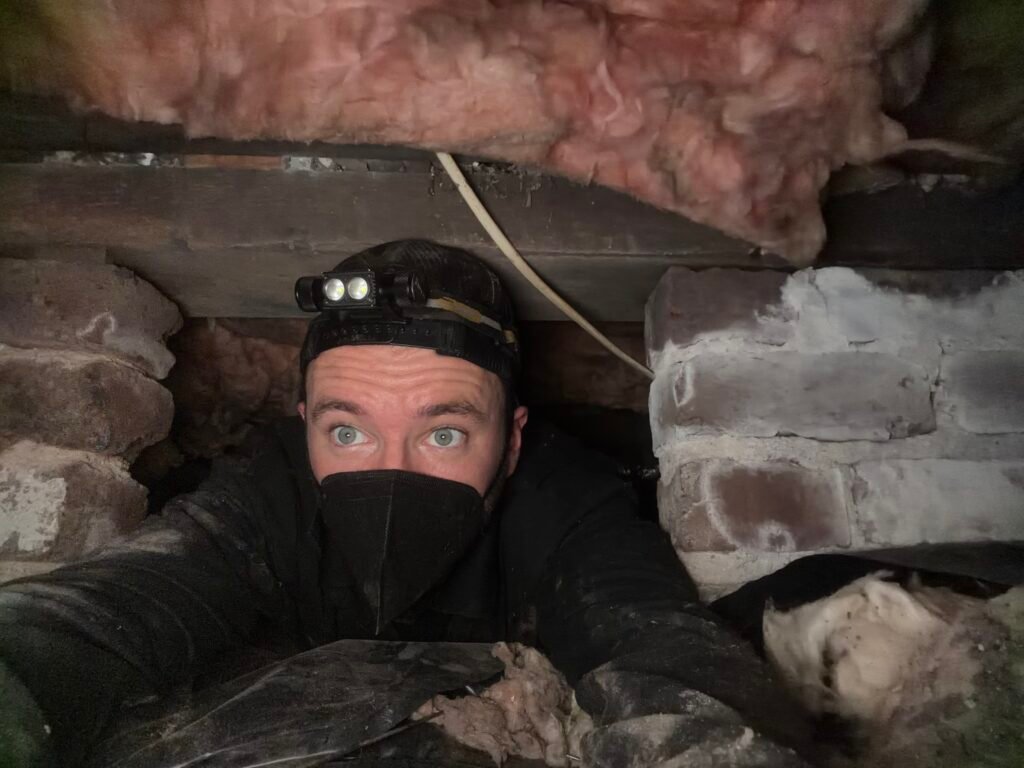 Home inspector harrison crawling into low clearance crawl space access hatch.