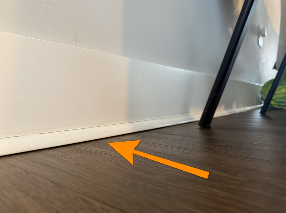 Gap between bottom baseboard trim and wood flooring indicating floor sag.
