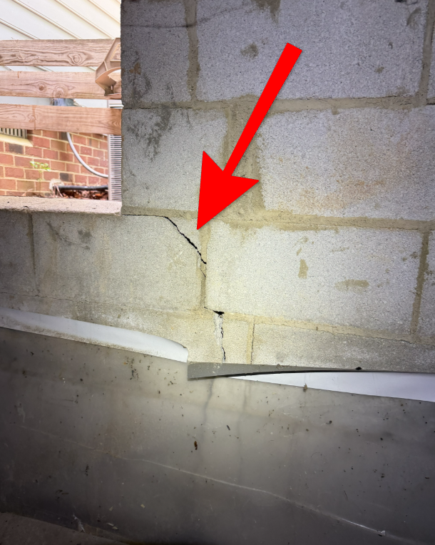 Large structural crack in foundation masonry beside crawl space access door.