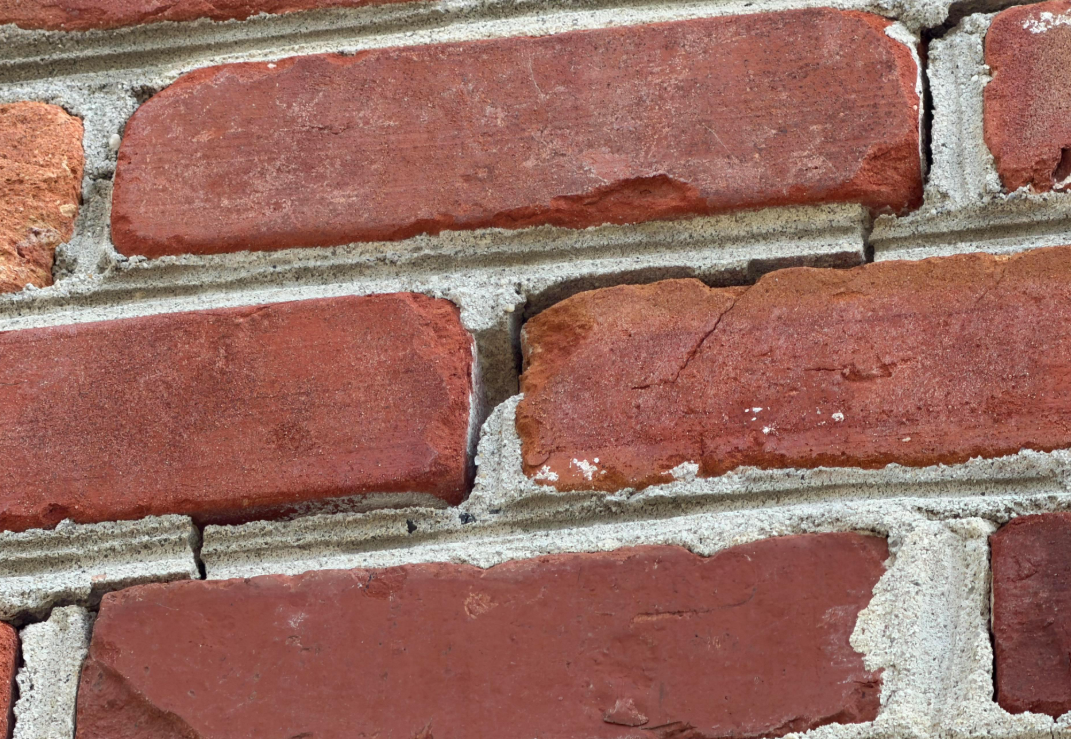 Close-up of active diagonal stair-step crack in exterior masonry mortar.