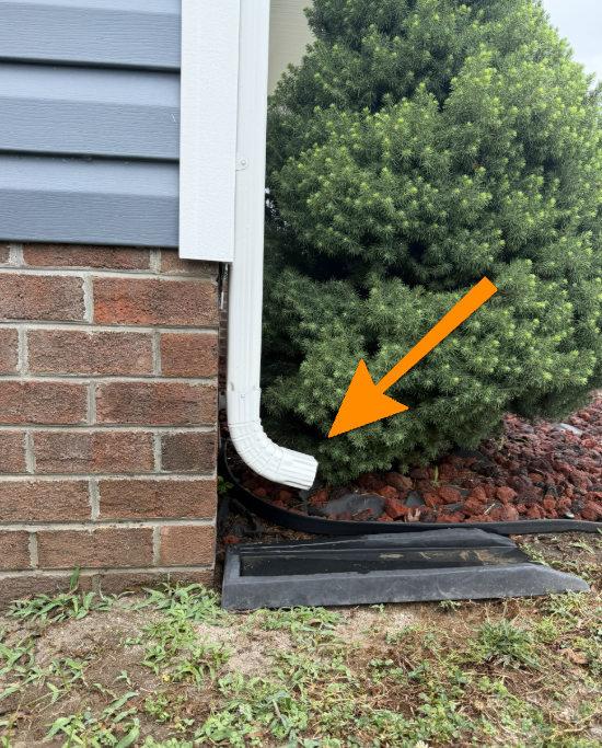 Gutter downspout discharging water directly next to foundation on negative grade.