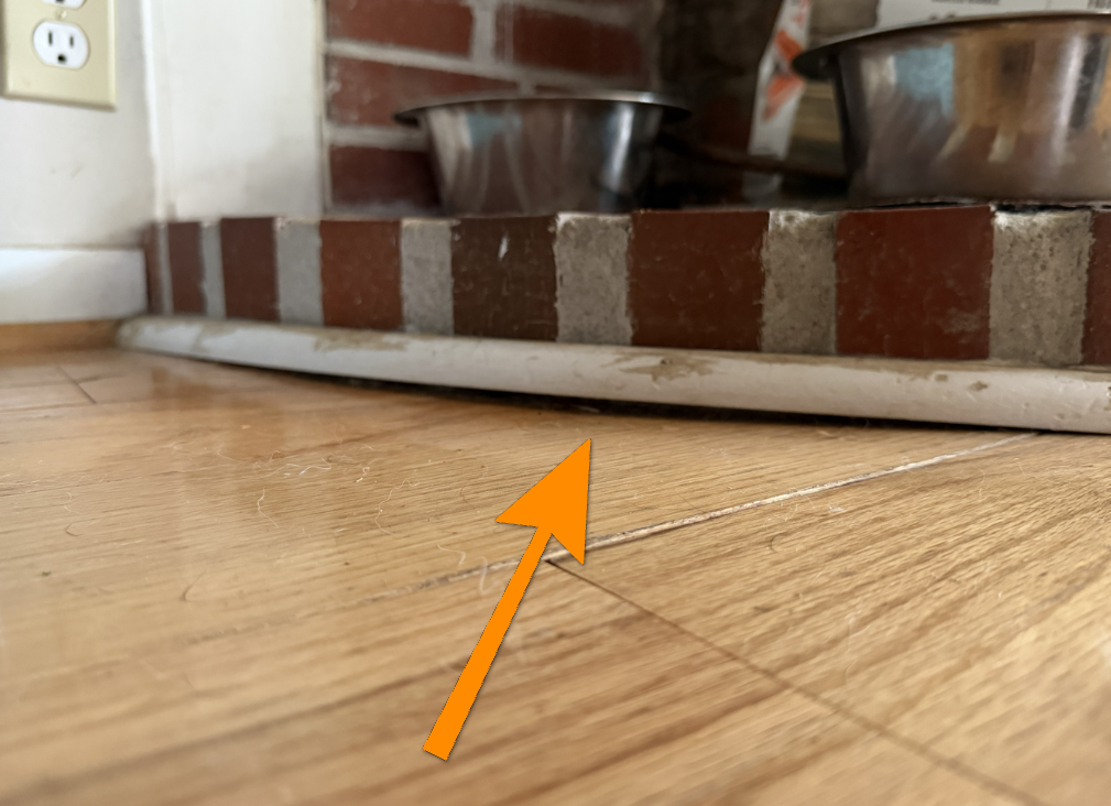 Gap beneath fireplace hearth tile indicating subfloor settlement or sagging.