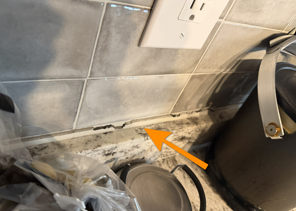Cracked kitchen countertop sealant gap suggesting underlying floor settlement.
