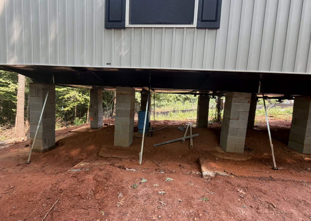 Manufactured home supported by improper dry-stacked concrete piers near sloped grade.