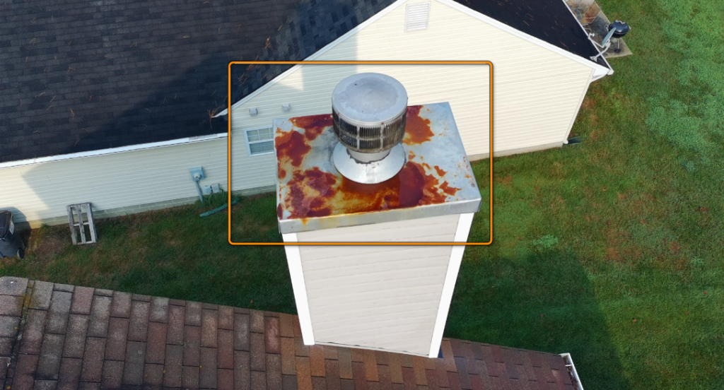 Rusted metal chimney cap atop brick flue structure.
